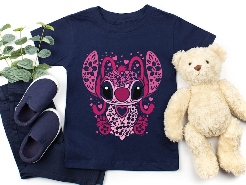 May include: A navy blue t-shirt with a pink and white floral design of Stitch from Lilo & Stitch. The design features hearts and flowers.