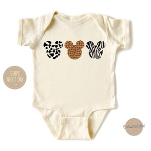 May include: A cream-colored baby onesie with three animal print Mickey Mouse ears. The ears are a black and white cow print, a brown giraffe print, and a black and white zebra print.