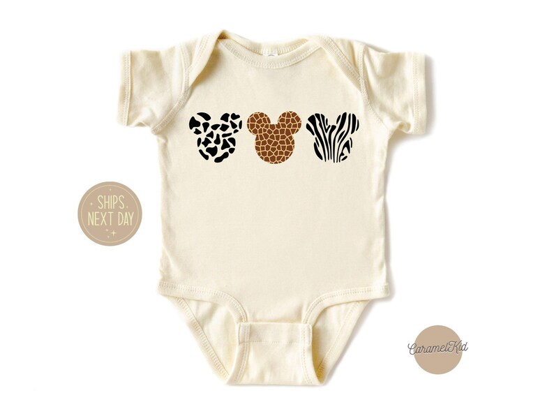 May include: A cream-colored baby onesie with three animal print Mickey Mouse ears. The ears are a black and white cow print, a brown giraffe print, and a black and white zebra print.