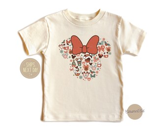 Puede incluir: Una camiseta de color crema con un lazo rojo y una silueta de Minnie Mouse con temática navideña compuesta por varios iconos navideños. La silueta incluye un árbol de Navidad, bastones de caramelo, adornos y otros elementos festivos.