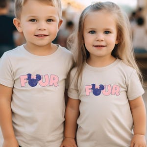 K&ouml;nnte beinhalten: Zwei Kinder tragen hellbeige T-Shirts mit dem Wort "FOUR" in rosa Buchstaben und einem blauen Mickey Mouse Kopf-Motiv.