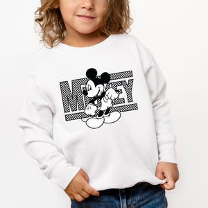 May include: White sweatshirt with a black and white graphic of Mickey Mouse and the word "Mickey" printed on it.