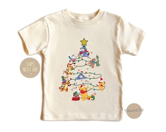 May include: A white t-shirt with a Christmas tree design featuring Winnie the Pooh and his friends. The tree is decorated with lights, ornaments, and candy canes. The characters are all smiling and wearing festive attire.