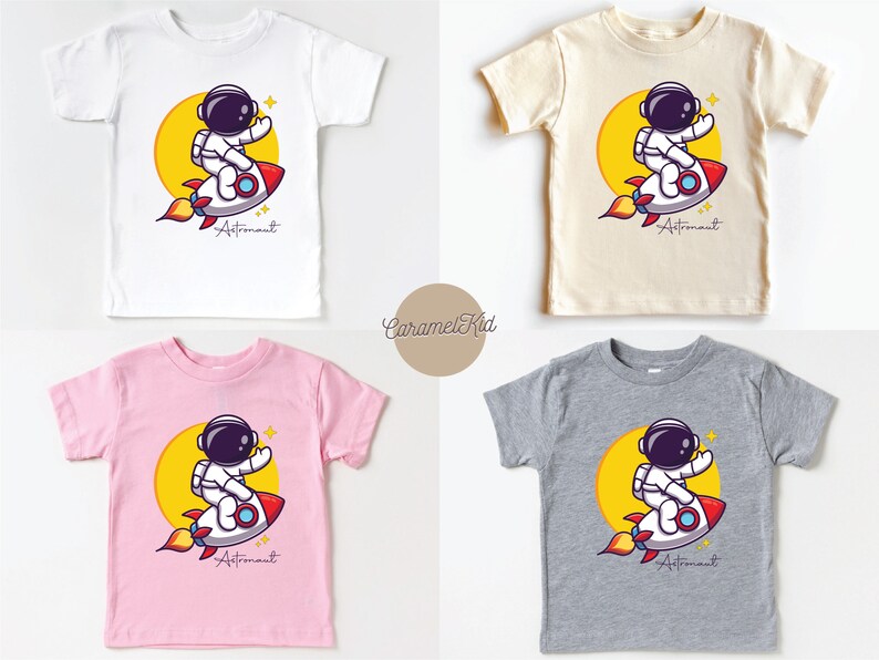 May include: Four different color t-shirts featuring a cartoon astronaut riding a rocket with the word "Astronaut" printed below. The shirts are white, beige, pink, and gray.