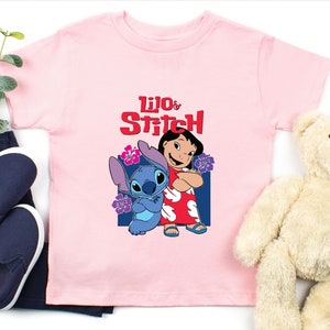 May include: Pink t-shirt with a graphic of Lilo and Stitch from the Disney movie. The text "Lilo & Stitch" is printed in red on the shirt.