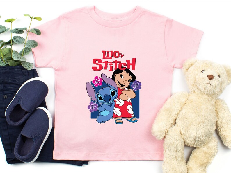 May include: Pink t-shirt with a graphic of Lilo and Stitch from the Disney movie. The text "Lilo & Stitch" is printed in red on the shirt.