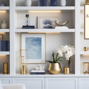 May include: A white bookshelf with multiple shelves filled with decorative items, including vases, books, and artwork. The shelves are lit with LED lights. The bookshelf is a great backdrop for a Zoom meeting.