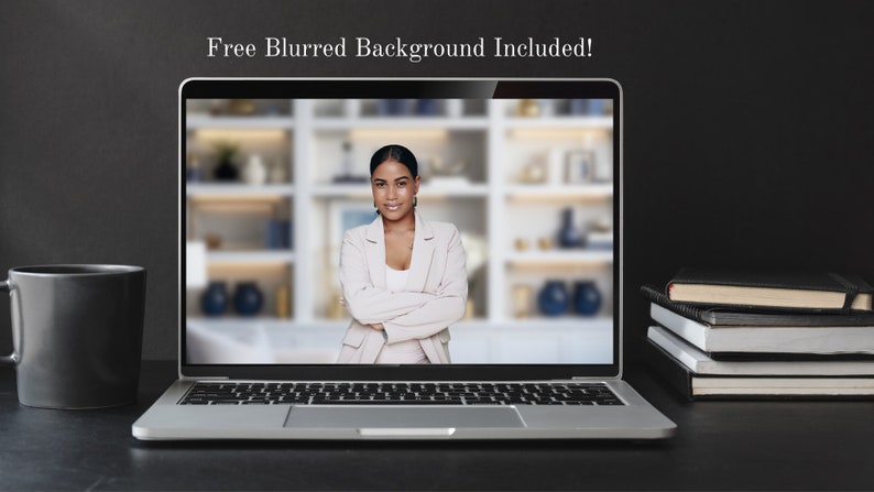 May include: A silver laptop computer with a black screen showing a woman in a light pink blazer with her arms crossed. The woman is smiling and looking at the camera. The background is blurred and shows a bookshelf with various items on it. The laptop is on a black surface with a black mug and a stack of books to the right.