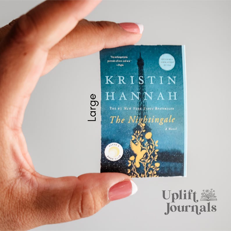 May include: A paperback book with a blue cover featuring a gold illustration of a bird and a tower. The title of the book is "The Nightingale" by Kristin Hannah. The book is a #1 New York Times Bestseller.
