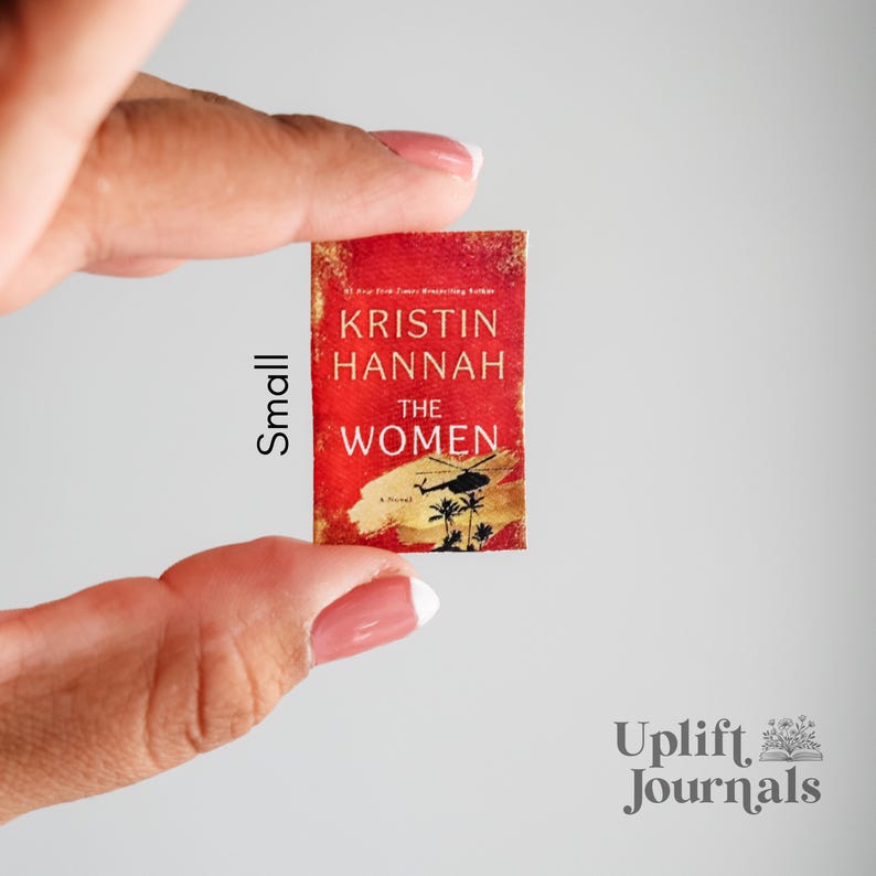 May include: A small paperback book with a red cover and gold lettering. The title is "The Women" by Kristin Hannah.