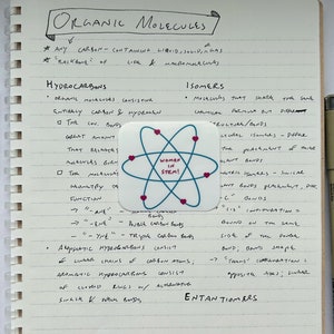 May include: A notebook page with handwritten notes about organic molecules, including a definition of hydrocarbons and a section on isomers. A sticker with the text "Women in STEM!" is placed on the page.