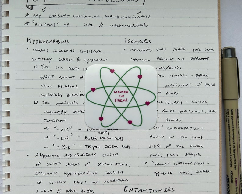 May include: A handwritten page of notes on hydrocarbons and isomers in chemistry. A green and pink sticker with the text "Women in STEM!" is attached to the page.