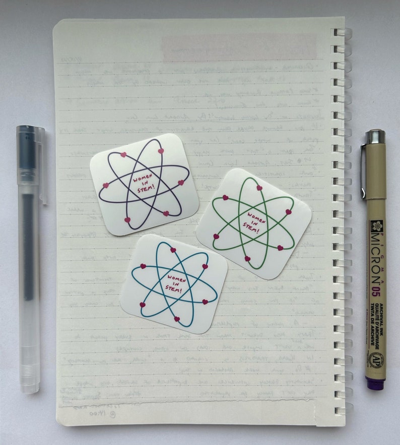 May include: Three square stickers with a pink heart and atom design. Each sticker says "Women in STEM!" in pink text.