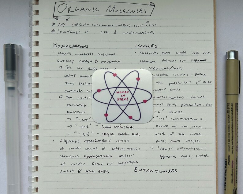 May include: A handwritten page of notes on organic molecules, with a sticker of an atom with the words "Women in STEM!" in the center. The notes discuss hydrocarbons, isomers, and enantiomers.