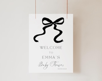 May include: A white sign with a black bow and the text "Welcome to Emma's Baby Shower 04/04/2024".