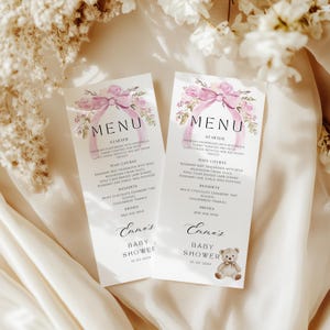 May include: Two pink and white baby shower menu cards with a watercolor floral design and a pink bow. The text on the cards reads "Emma's Baby Shower" and includes a list of food and drinks. The date of the shower is 01-03-2024.