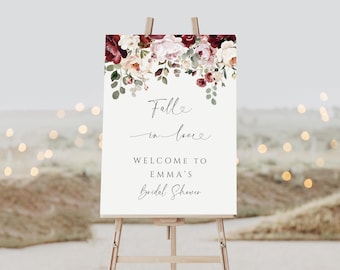 Puede incluir: Un letrero blanco sobre un caballete de madera con el texto "Fall in love" y "Welcome to Emma's Bridal Shower". El letrero está decorado con arreglos florales burdeos, rosas y blancos.
