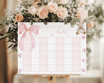 Op de afbeelding: Een roze en witte baby shower kalender met de tekst "Guess the due date". De kalender heeft een roze strik, een teddybeer en bloemmotieven. Het wordt gepresenteerd op een houten ezel.