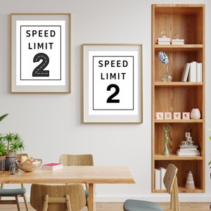 Puede incluir: Dos impresiones enmarcadas en blanco y negro con el texto "Speed Limit 2" sobre un fondo blanco. Las impresiones est&aacute;n colgadas en una pared blanca sobre una mesa de madera con sillas.