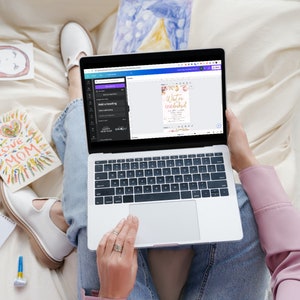 Puede incluir: Una persona sentada en una cama con un port&aacute;til abierto. La pantalla del port&aacute;til muestra una plantilla de dise&ntilde;o para una invitaci&oacute;n de fiesta "Winter One-derland". La invitaci&oacute;n tiene un fondo rosa con letras doradas y detalles florales.