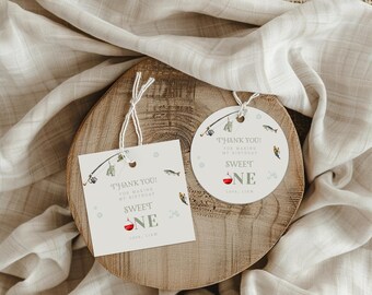 May include: Two fishing-themed gift tags, one square and one round, with the text "THANK YOU! FOR MAKING MY BIRTHDAY SWEET ONE" and a fishing rod illustration. The tags are on a wooden slice with a neutral fabric background.