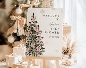 May include: A white rectangular welcome sign for a baby shower on a wooden easel. The sign features a watercolor illustration of a green Christmas tree decorated with pink bows, gold snowflake accents, and the text Welcome to Jessica's Baby Shower 04/04/2024.
