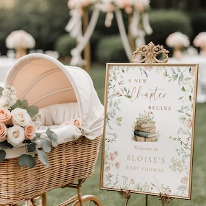 Könnte beinhalten: Ein Babywagen im Vintage-Stil mit pfirsichfarbenem Innenraum und Blumenschmuck. Ein Schild mit goldenem Rahmen verkündet "Ein neues Kapitel beginnt" und heißt die Gäste von Eloises Babyparty willkommen. Die Szene spielt sich im Freien ab.