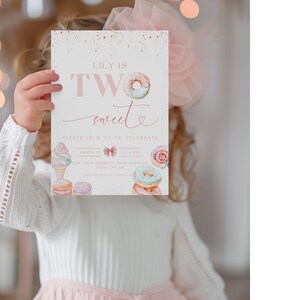 Op de afbeelding: Een roze en witte verjaardagsuitnodiging met de tekst "Lily is Two sweet" en een donut-illustratie. De uitnodiging heeft een roze strik en andere zoete lekkernijen zoals ijshoorns en cupcakes.