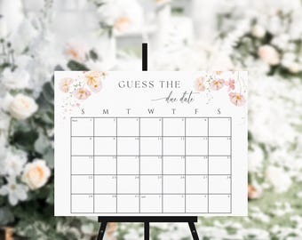 Può includere: Un cartello bianco con un disegno floreale e il testo "GUESS THE due date" sopra una griglia di calendario. Il cartello è su un cavalletto nero.
