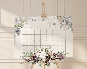 May include: A white calendar with a floral design border. The calendar is labeled "Guess the Due Date" and has the days of the week labeled S, M, T, W, T, F. The calendar is on an easel.