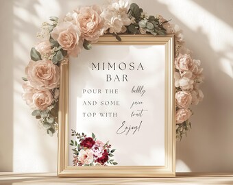 May include: A framed sign with the words "Mimosa Bar" in elegant black font. The sign is surrounded by a wreath of pink and white flowers. The text on the sign reads "Pour the bubbly, and some juice, top with fruit, Enjoy!"