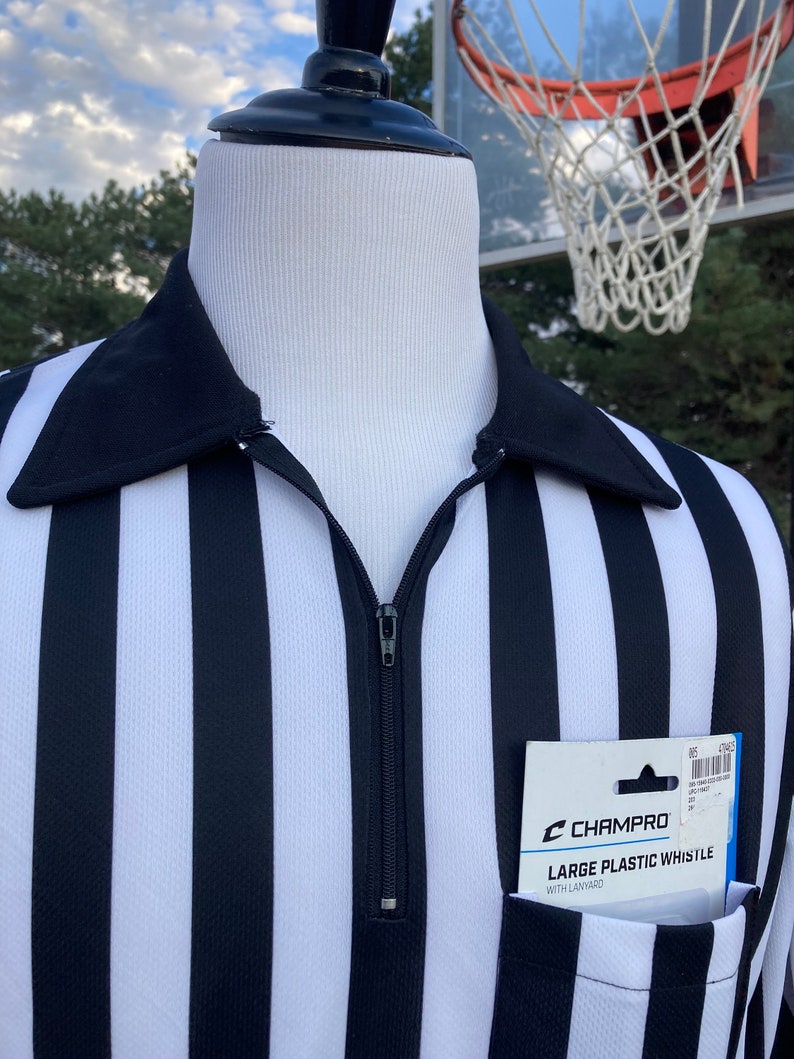 May include: Black and white striped referee shirt with a zipper and a pocket. The pocket contains a package of a Champro large plastic whistle with lanyard.