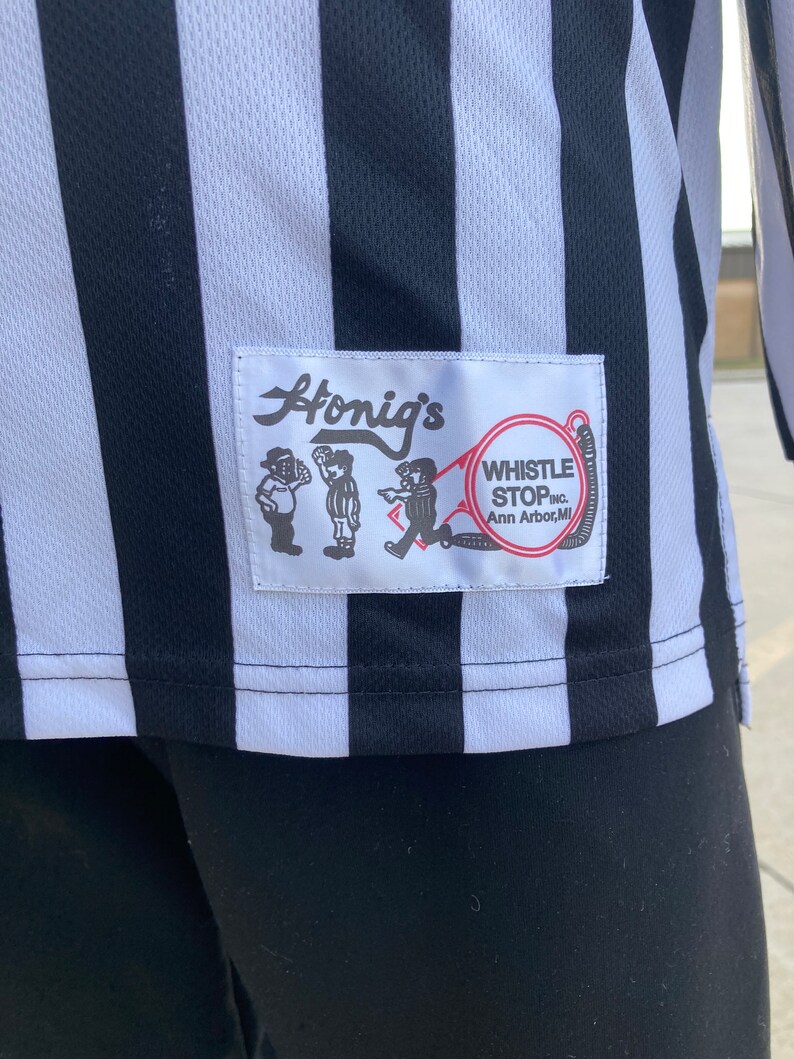 May include: A black and white striped referee shirt with a patch that says "Honig's Whistle Stop Inc. Ann Arbor, MI"