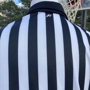 May include: Black and white striped referee shirt with a small white logo on the back.