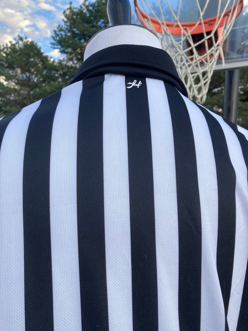 May include: Black and white striped referee shirt with a small white logo on the back.