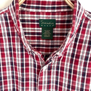 May include: A red, white, and blue plaid button-down shirt with a Scandia Woods label. The label says "100% Cotton FN 81700 Made in India Reverse for Care XL-RG 5335607".
