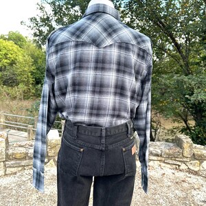 May include: A black and white plaid long-sleeve shirt and black denim jeans. The shirt has a classic western style with a pointed yoke and buttoned cuffs. The jeans are a dark wash with a high waist and a straight leg.