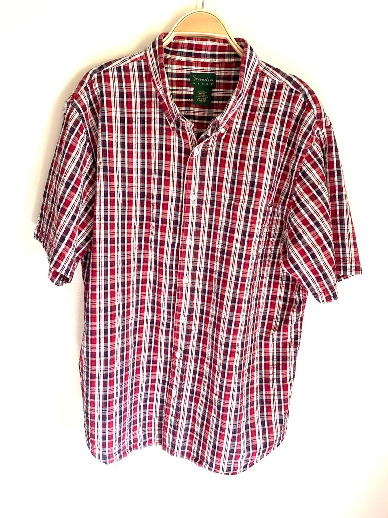 May include: A red, white, and blue plaid short-sleeved button-down shirt with the brand name "Granda" on the label.