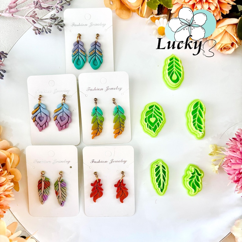 May include: A selection of feather-shaped earrings and leaf-shaped clay cutters. The earrings, on white cards marked "Fashion Jewelry", display vibrant colours like teal, purple, orange, and red. The clay cutters are green. The earrings are for pierced ears.