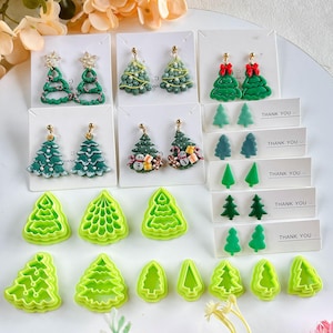 May include: A collection of Christmas-themed earrings and green plastic tree-shaped cutters. The earrings feature various designs, including Christmas trees with star toppers, bows, and snowman details. The cutters are in different tree shapes.