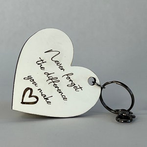 May include: A white heart-shaped keychain with the engraved text "Never forget the difference you make" and a small heart symbol. The keychain has a silver key ring and a small charm.