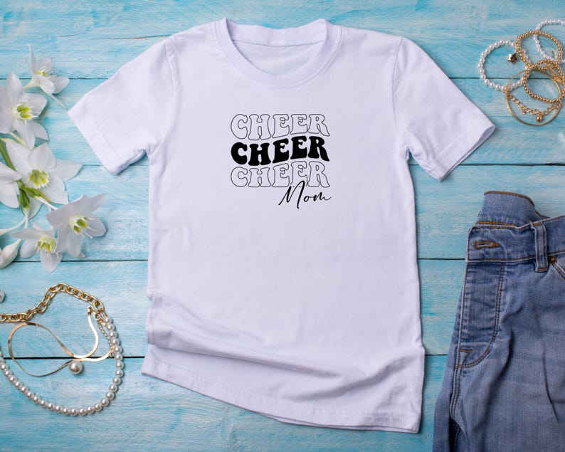 May include: White t-shirt with black text that reads "Cheer Cheer Cheer Mom" in a retro font.
