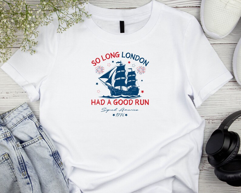 May include: White t-shirt with a blue and red graphic of a ship sailing away from a city skyline. The text "So Long London Had A Good Run Signed America 1776" is printed on the shirt.