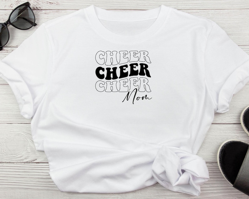 May include: White t-shirt with the text "Cheer Cheer Cheer Mom" in black retro font.