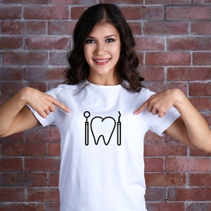 May include: A white t-shirt with a black graphic of a tooth, a dental mirror, and a dental pick. The person wearing the shirt is pointing at the graphic.