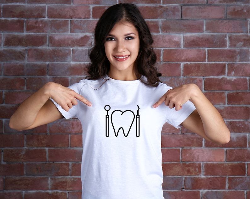 May include: A white t-shirt with a black graphic of a tooth, a dental mirror, and a dental pick. The person wearing the shirt is pointing at the graphic.