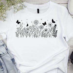 May include: White t-shirt with a black line drawing of a field of flowers and butterflies.