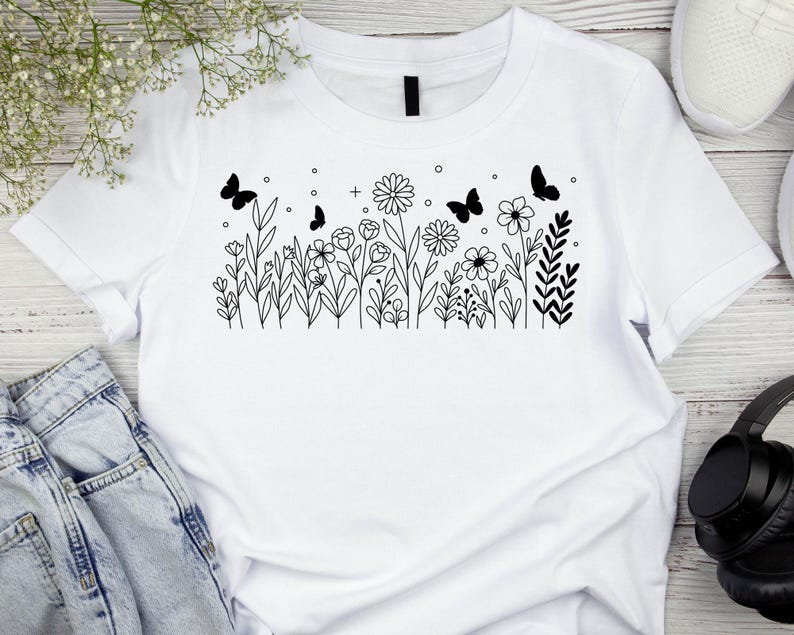 May include: White t-shirt with a black line drawing of a field of flowers and butterflies.