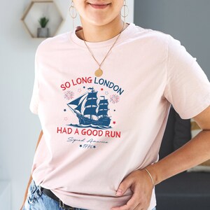 May include: A pink t-shirt with a blue and white ship graphic and the text "So Long London Had a Good Run Signed America 1776".