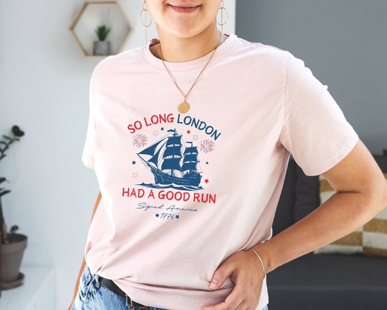 May include: A pink t-shirt with a blue and white ship graphic and the text "So Long London Had a Good Run Signed America 1776".